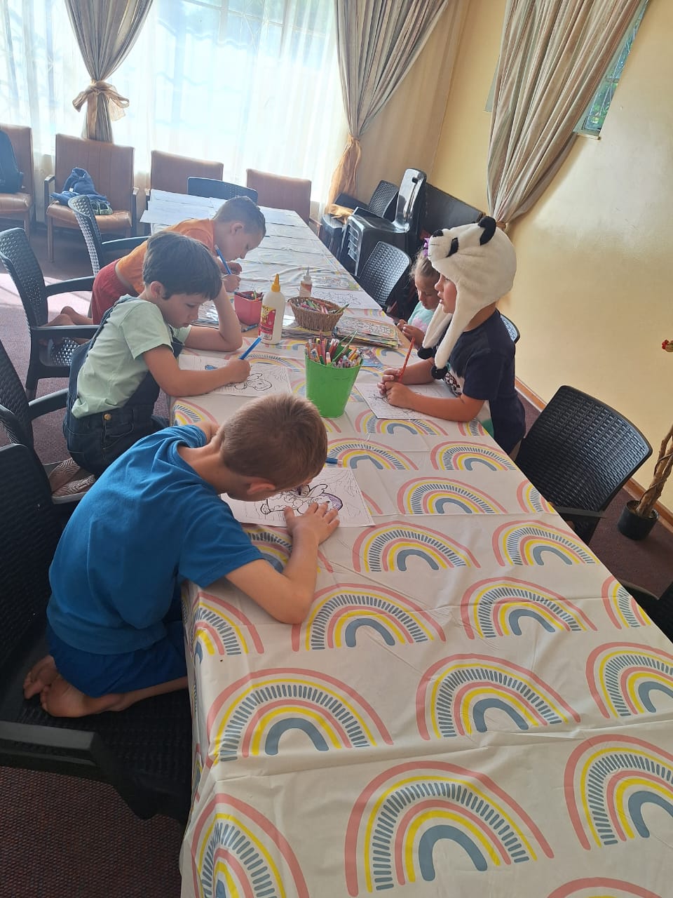 Children colouring in pictures together around a table with a rainbow tablecloth