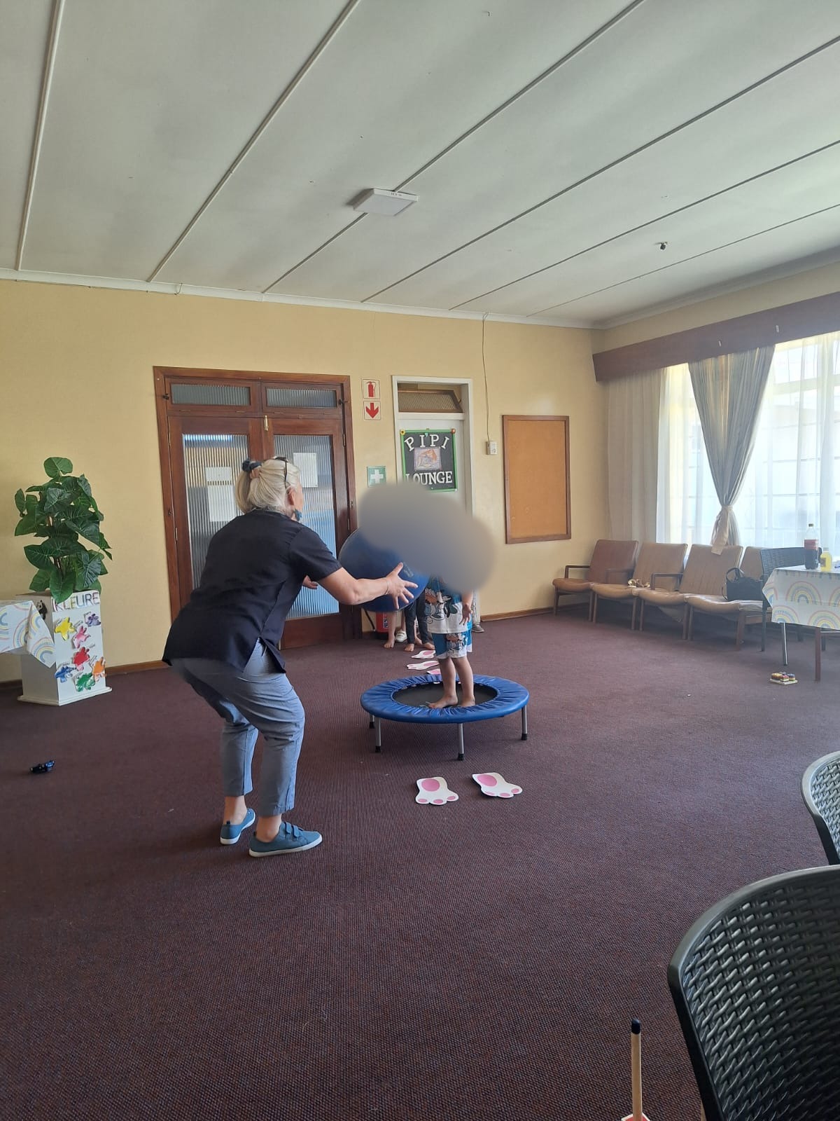 Karen leading a ball and trampoline activity, with children's faces blurred for privacy