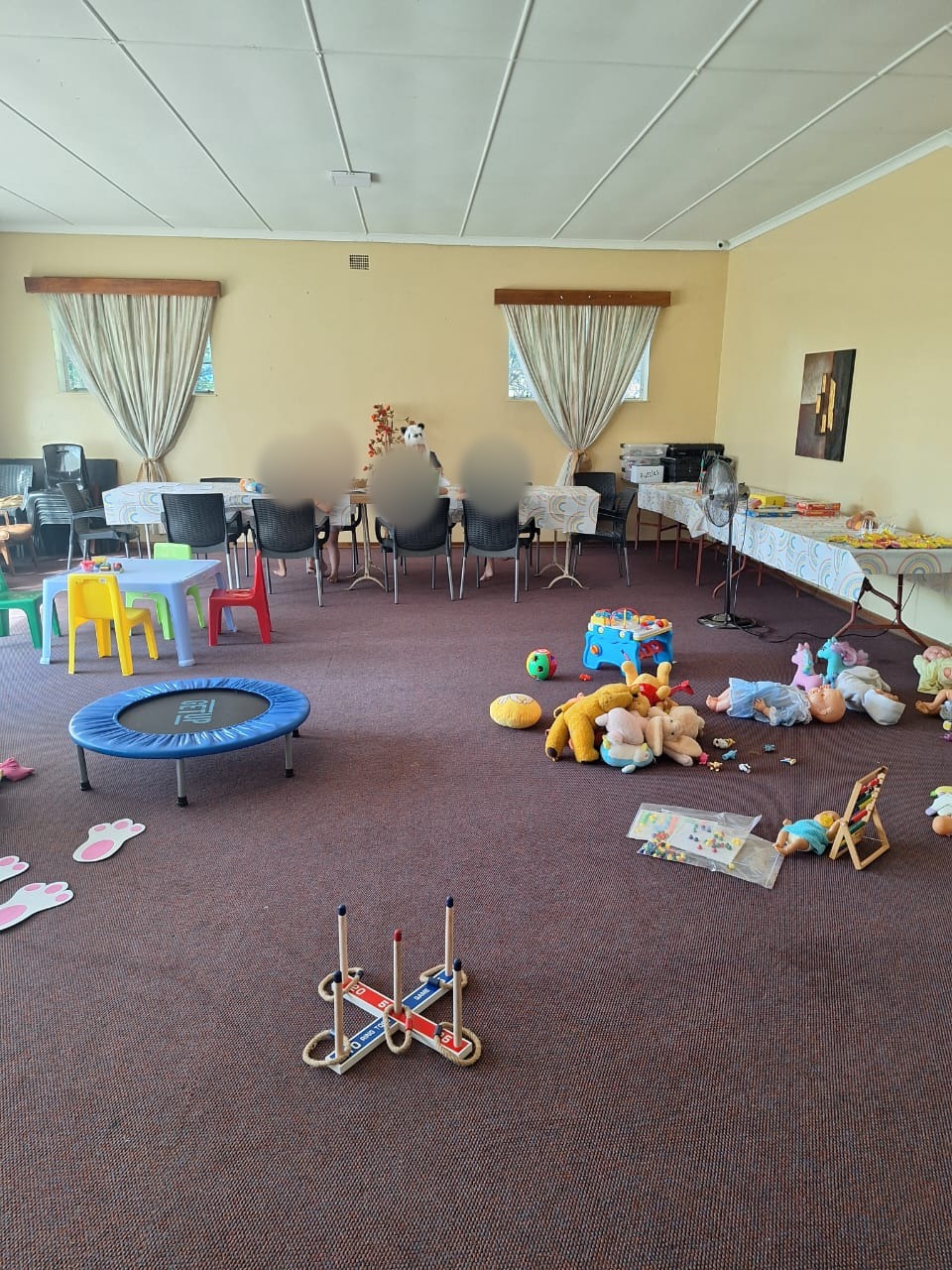 A group play space with toys, games and children at a colouring table, faces blurred for privacy