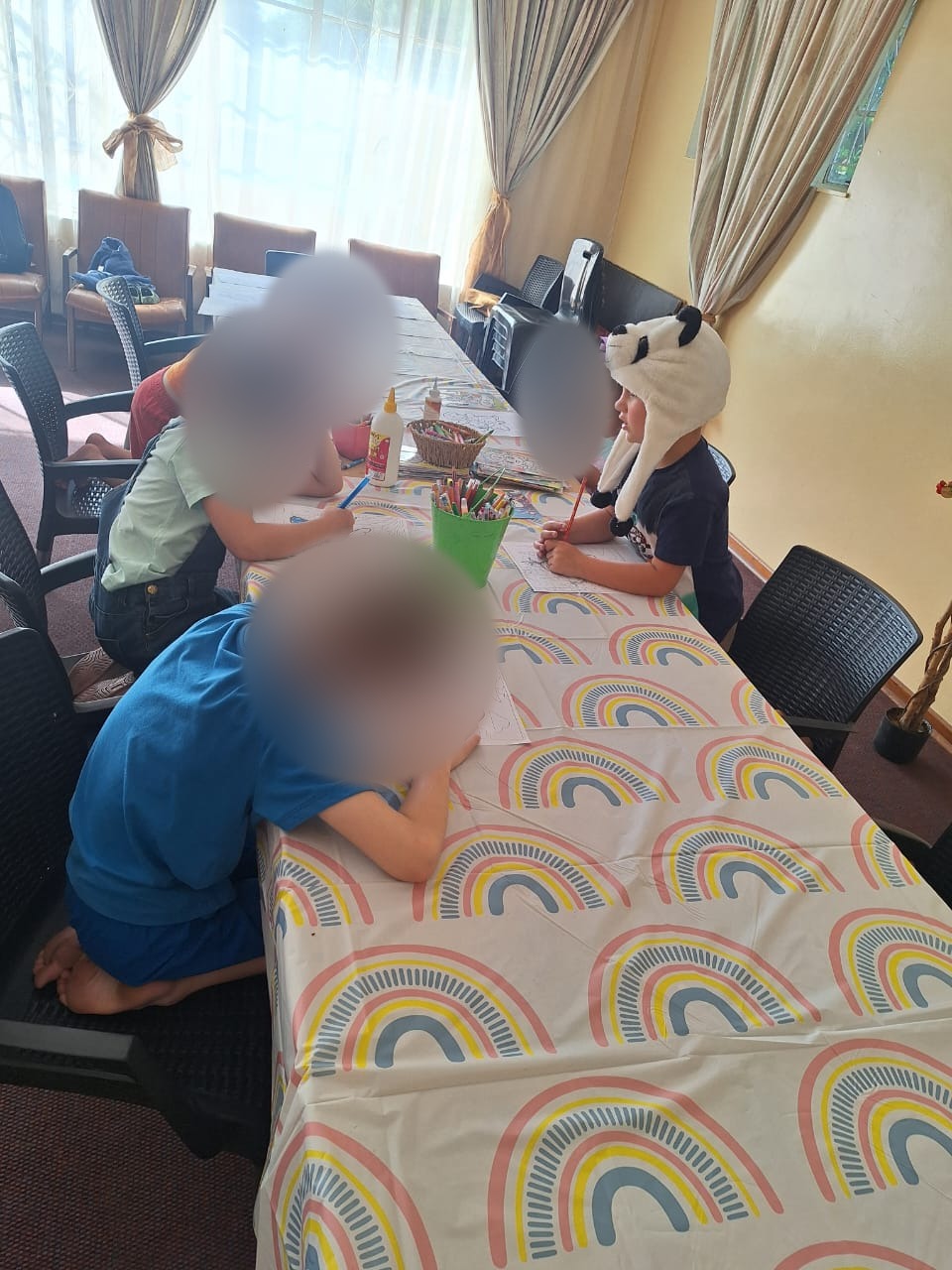 Children colouring around a rainbow-covered table with Karen; children's faces blurred